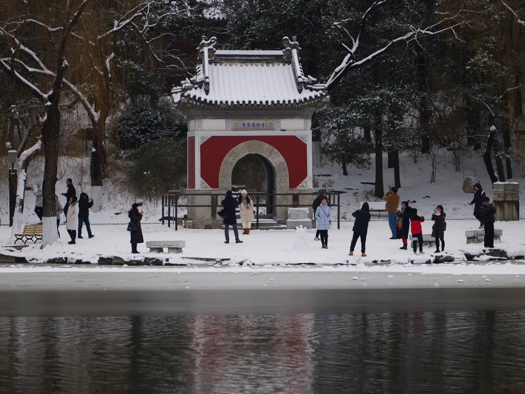 Visitors gathered around a red traditional gate beside a frozen lake after snowfall