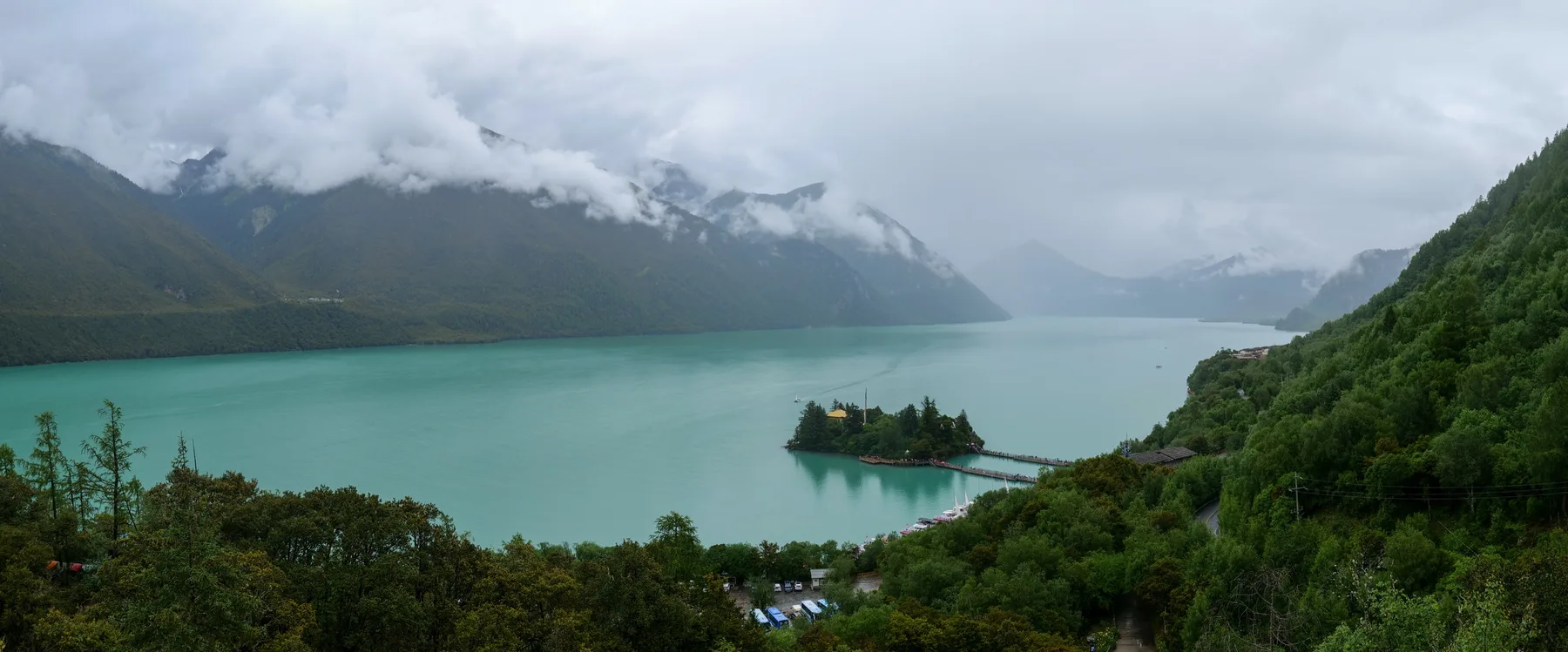 A turquoise mountain lake and small island beneath low clouds