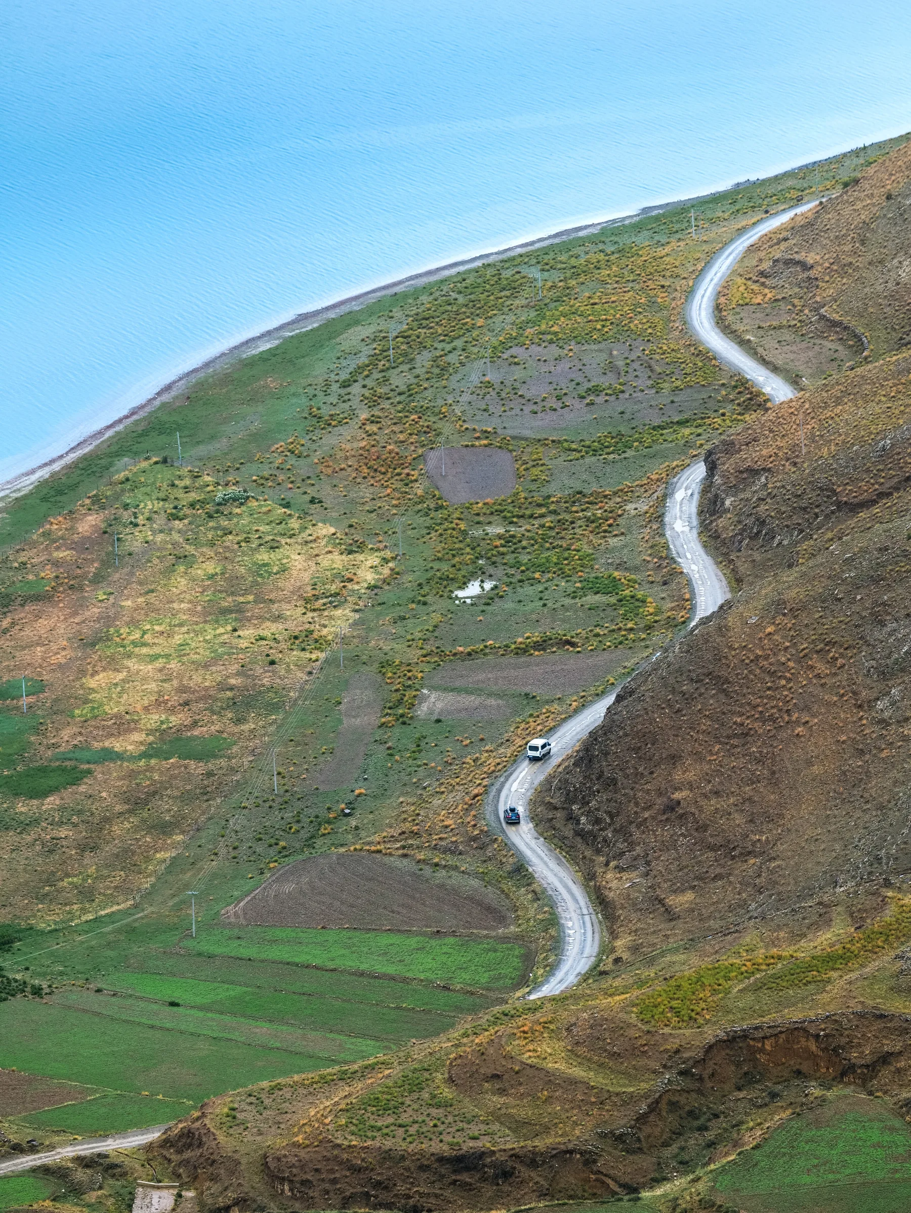 A winding road crossing patchwork fields on a highland slope