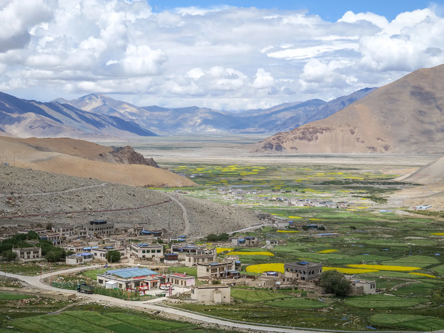 A high mountain valley with a village and yellow fields beneath towering clouds