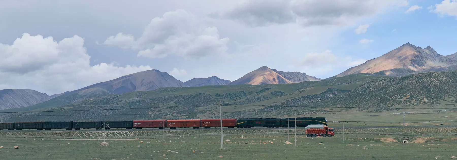 A long freight train crossing a high plateau beneath layered mountains and storm clouds