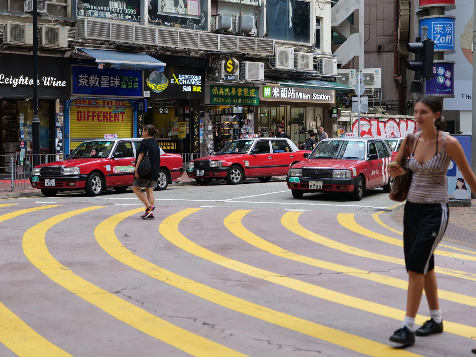 Red taxis and pedestrians crossing a street lined with dense shop signs in Hong Kong