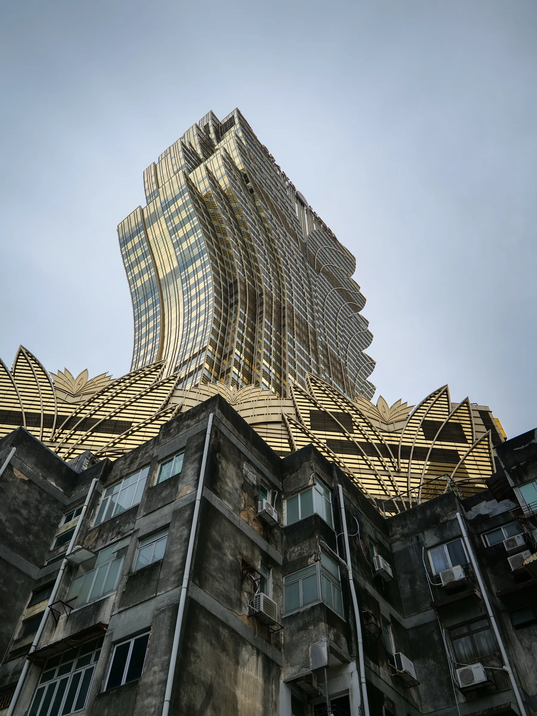 A gold-toned high-rise rising behind weathered residential buildings