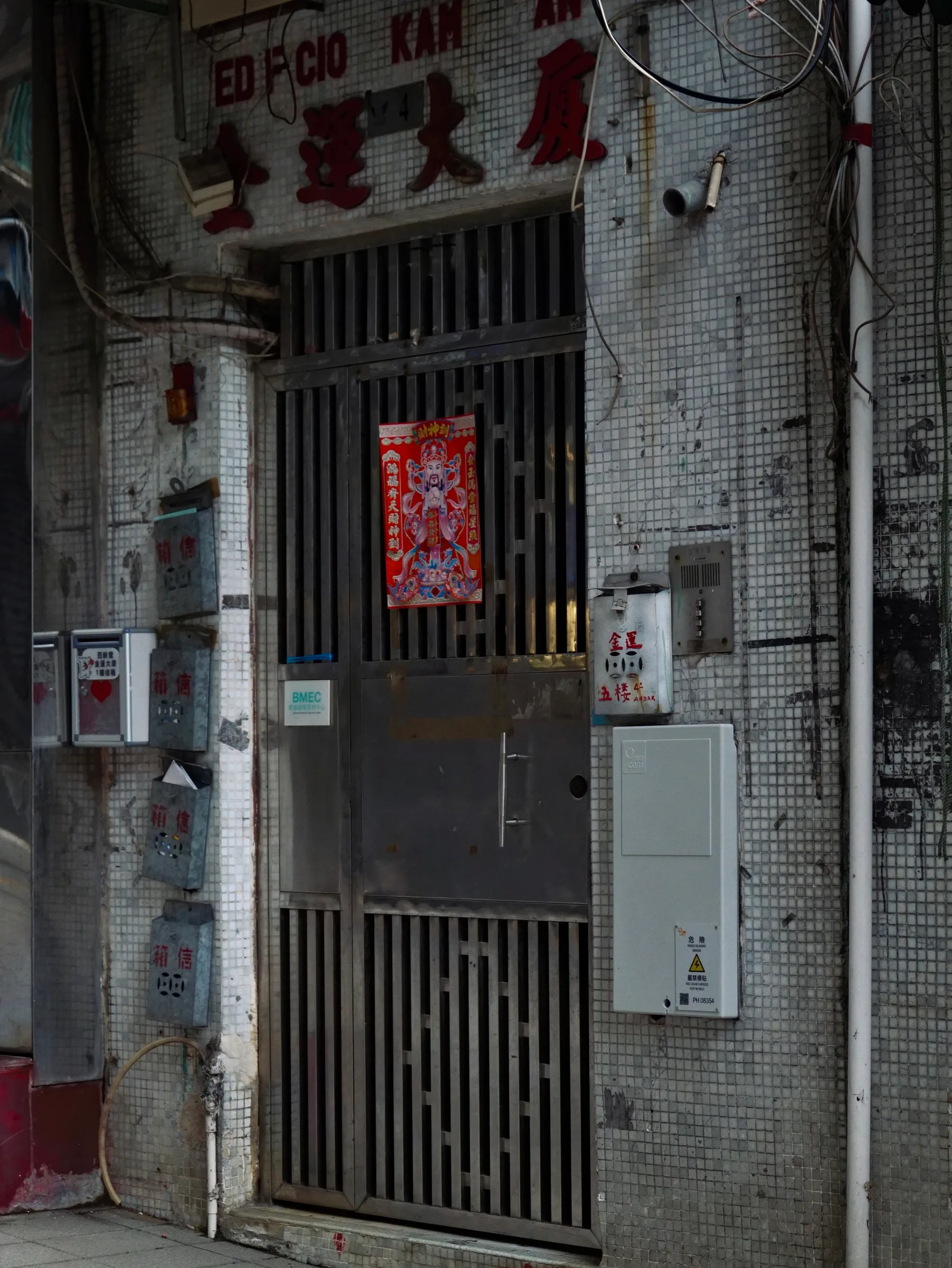 A weathered tiled doorway with metal mailboxes, exposed wires, and a red door-god poster
